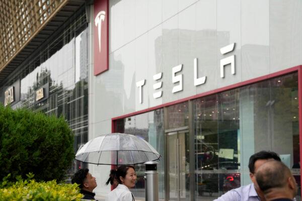 Workers chat under an umbrella outside the Tesla showroom in Beijing, China, on May 30, 2023. (AP Photo/Ng Han Guan)