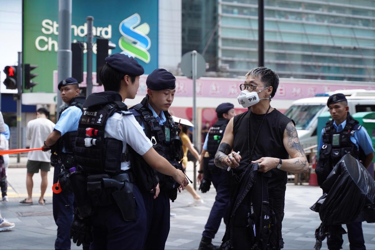 A male wearing a black T-shirt and a mask with the words “Hong Kong Add Oil” was stopped and searched by the police. (Sung Pi-lung/ The Epoch Times)