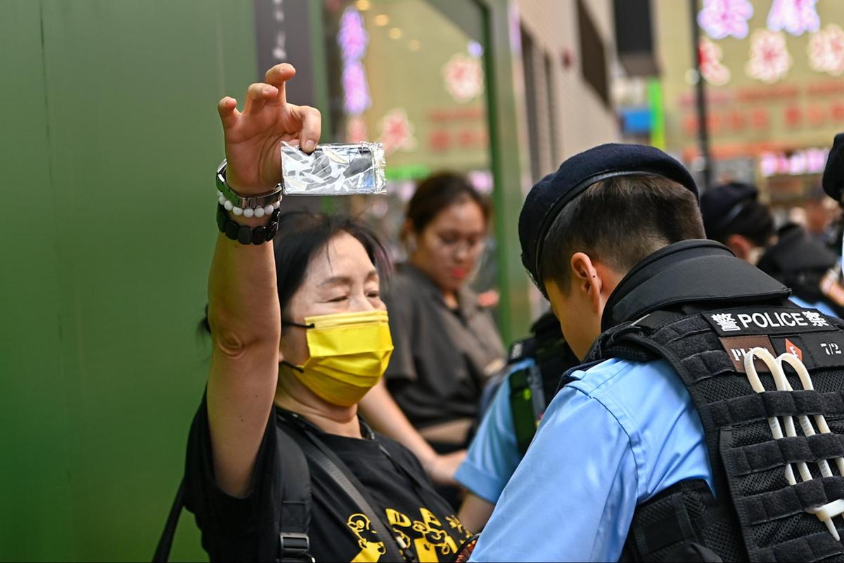 A woman wearing a yellow mask was holding up a card that read “Conscience” while being searched by the police. (Sung Pi-lung/ The Epoch Times)