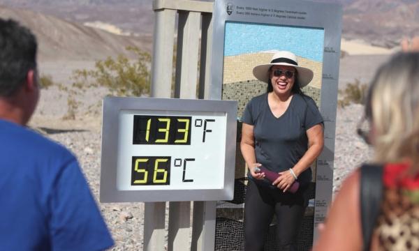 Melanie Anguay, di Las Vegas, sta per una foto accanto a un display digitale di una lettura non ufficiale del calore al Furnace Creek Visitor Center durante un'ondata di caldo nel Parco nazionale della Death Valley nella Death Valley, California, il 16 luglio 2023. (Ronda Churchill/AFP tramite Getty Images)