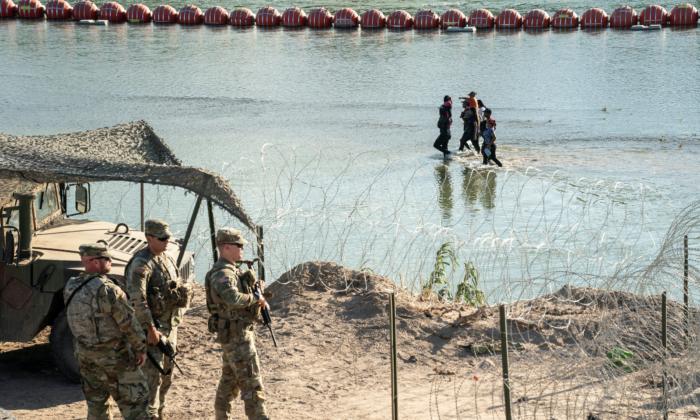 Illegal immigrants walk in the Rio Grande River between a floating fence and the river bank as they look for an opening on the concertina wire fence to land on U.S. soil in Eagle Pass, Texas, on July 24, 2023. (Go Nakamura/Reuters)