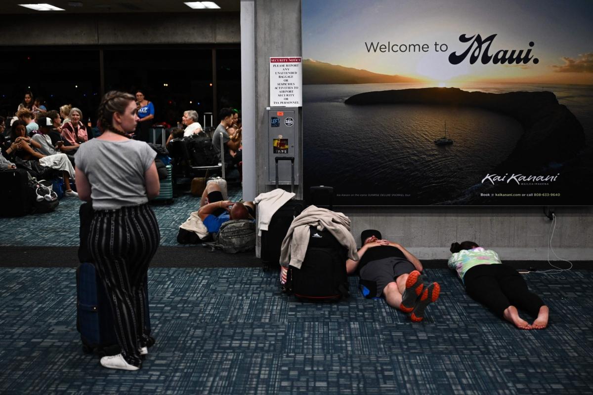 At Least 36 Killed in Hawaii Wildfires | USNN World News Passengers try to sleep below a "Welcome To Maui" billboard on the floor of the airport terminal while waiting for delayed and canceled flights off the island as thousands of passengers were stranded at the Kahului Airport in the aftermath of wildfires in western Maui in Kahului, Hawaii, on Aug. 9, 2023. (Patrick T. Fallon/AFP via Getty Images)
