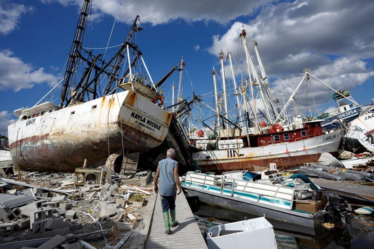One week after the passage of Hurricane Ian, Bruce Hickey walks along the waterfront, now littered with debris including shrimp boats, on San Carlos Island, Fort Myers Beach, Fla., on Oct. 5, 2022, (Rebecca Blackwell/AP Photo)