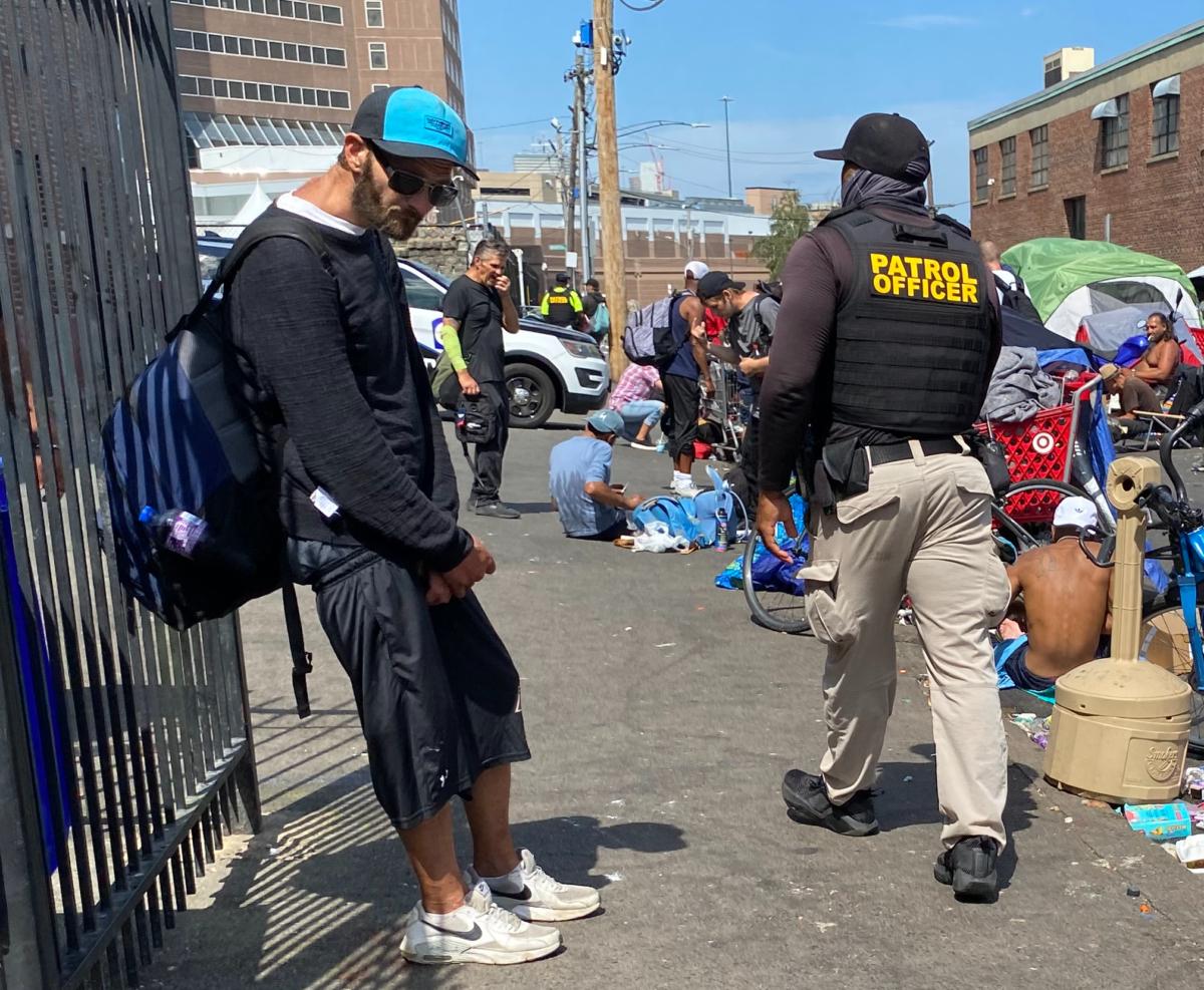 A patrol officer who worked for a private security company hired by the City of Boston walks through a homeless encampment in the city's South End district (Photo by Alice Giordano)