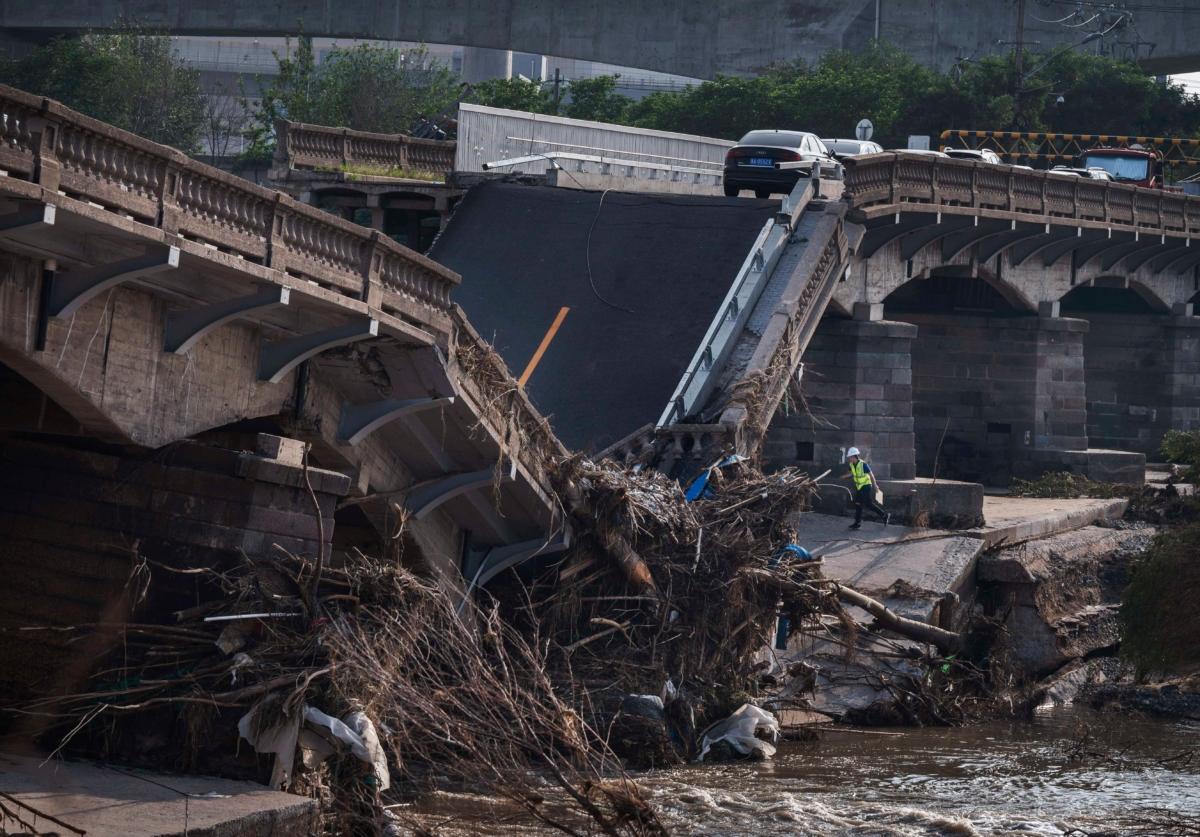 Abandoned cars are seen as a worker inspects a bridge that collapsed in recent days after a flash flood caused by heavy rainfall in Beijing on Aug. 4, 2023. The extreme rainfall from Typhoon Doksuri was the heaviest to hit Beijing in 140 years, inundating the capital and triggering flash floods and landslides. (Kevin Frayer/Getty Images)