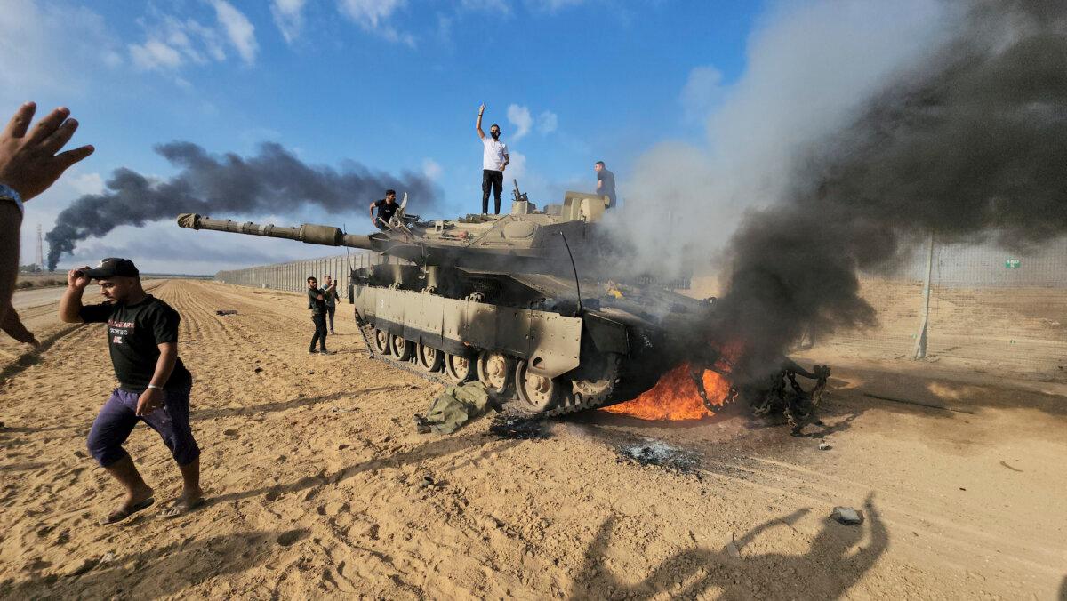 Palestinians celebrate by a destroyed Israeli tank at the Gaza Strip fence east of Khan Younis on Oct. 7, 2023. (Hassan Eslaiah/AP Photo)