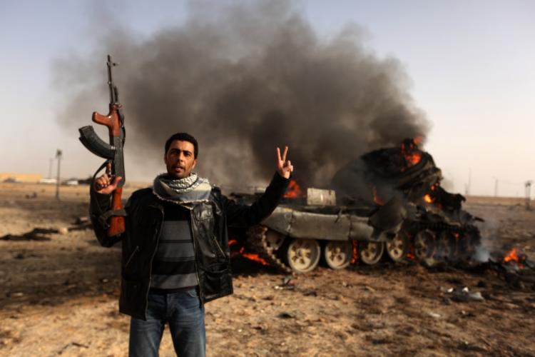 A Libyan rebel flashes a V-sign in front of burning tank belonging to loyalist forces bombed by coalition air force in the town of Ajdabiya on March 26, 2011. (Patrick Baz/AFP/Getty Images)