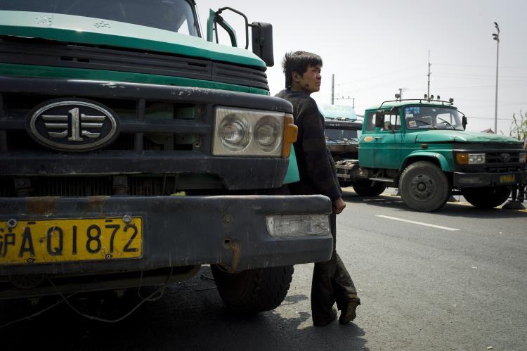 A Chinese mechanic waits by a container truck to be repaired near a cargo terminal in Shanghai on April 25. (Philippe Lopez/AFP/Getty Images)