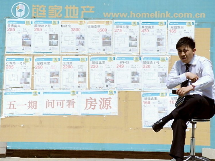 A property agent sitting in front of a board posting various property sales as he waits for house buyers by a street in Beijing. (Gou Yige/AFP/Getty Images)