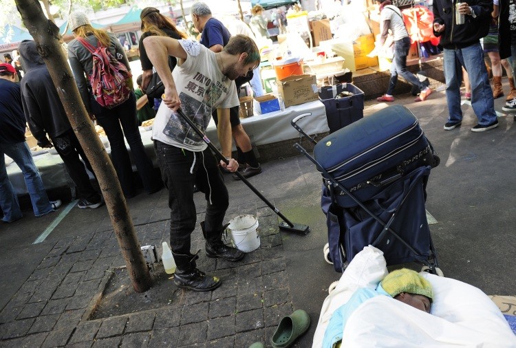 A volunteer scrubs the ground as a member of Occupy Wall Street sleeps after spending the night on Zuccotti Park near Wall Street in New York, October 11, 2011. (Emmanuel Dunad/AFP/Getty Images)