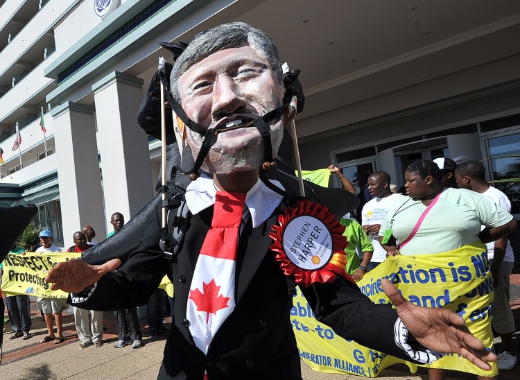 An activist wears a mask depicting the face of Canadian Prime Minister Stephen Harper