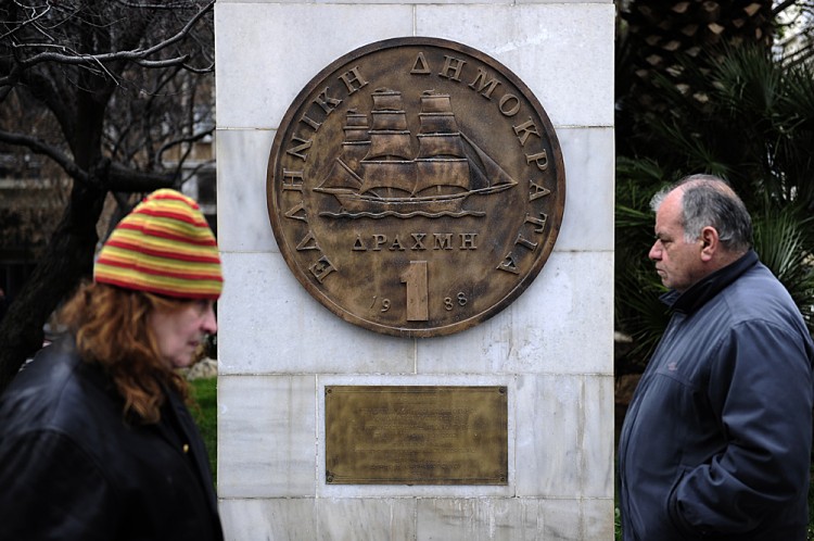 People walk past a monument featuring a replica of the last edition of the Greek currency, the drachma