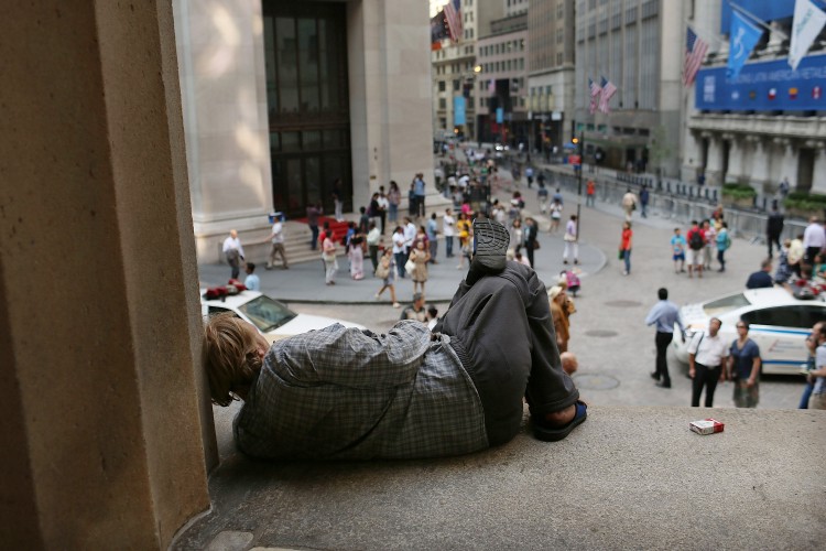 A homeless man rests along Wall Street in front of the New York Stock Exchange on June 22, in New York City
