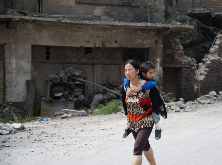 This photo taken on September 8, 2012 shows a woman carrying her child on her back along a street in Yiliang after two quakes hit the area on the border of southwestern Yunnan and Guizhou provinces an hour apart around the middle of the day followed by a string of aftershocks. (STR/AFP/GettyImages)