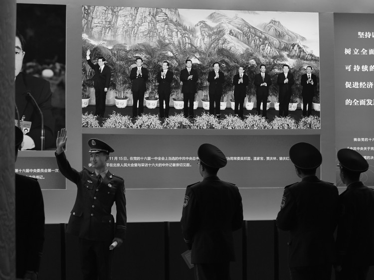 policeman poses for photo in front of the photo of Hu Jintao while visiting an exhibition