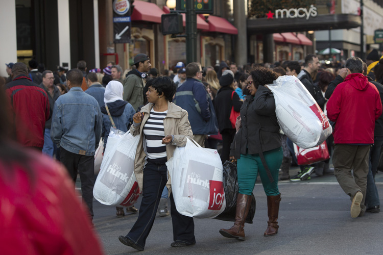 Women carry shopping bags across a crowded 34th Street in New York City 