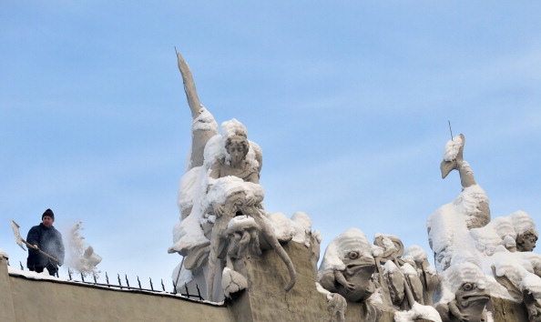 A communal worker cleans snow from sculptures adorning the roof of the 
