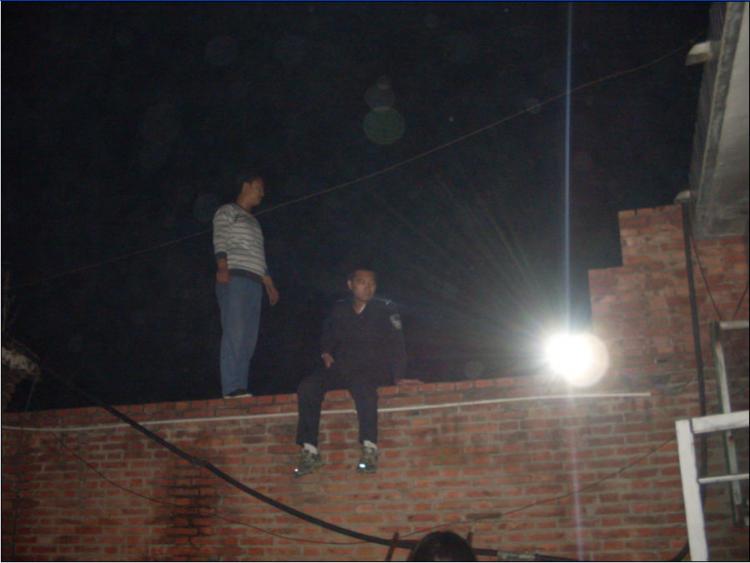 A uniformed man identified as Zhang Songwei, deputy head of the Yinliu Police Station, sits on a wall at night outside the girls' home. (Minghui.net)