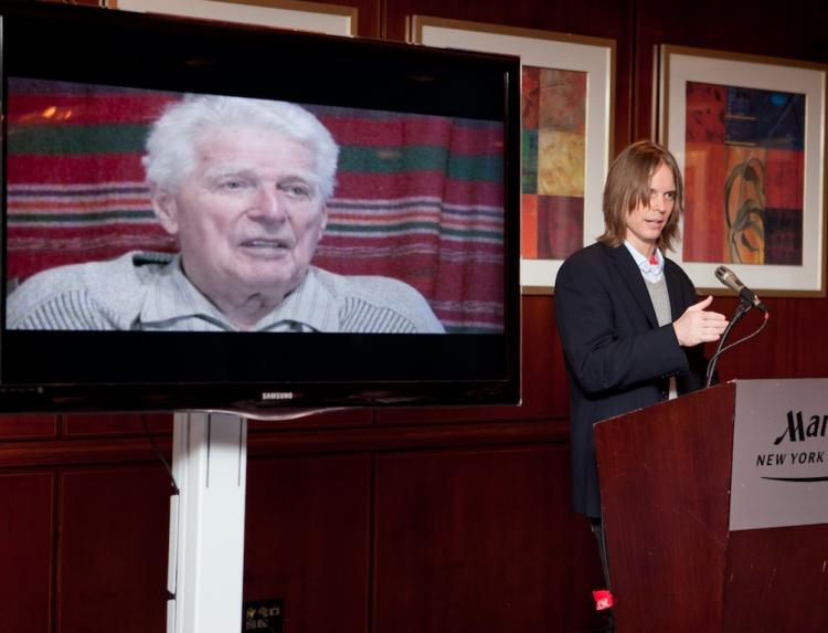 WAR CRIMES: American data broker Mark Gould (R) unveils video evidence which he says incriminates former Nazi colonel, 97-year-old Dr. Bernhard Frank (screen) as being guilty of genocide during World War II.  (The Epoch Times)
