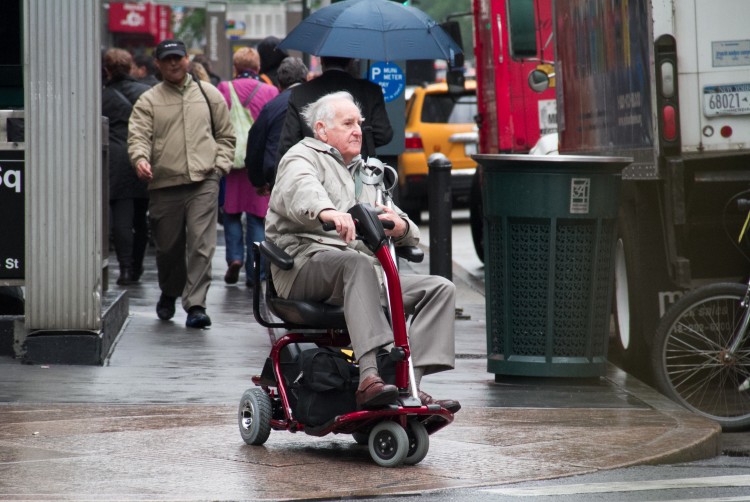 An elderly man drives a motorized wheelchair across the busy intersection of Sixth Avenue and 34th Street in Manhattan on April 26.