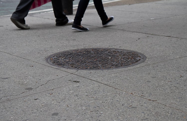 People walk by a manhole cover near Madison Square Park