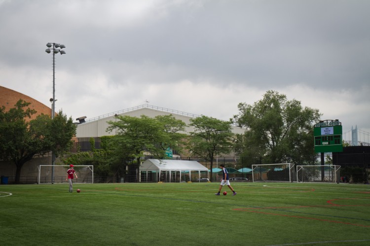 Boys play soccer on the field at the Asphalt Green Community Center in Manhattan on June 25, where the abandoned East 91st Street Trash Station rests in the background. The proposed plan would demolish the existing building and replace it with another 10 stories high. (Benjamin Chasteen/The Epoch Times)