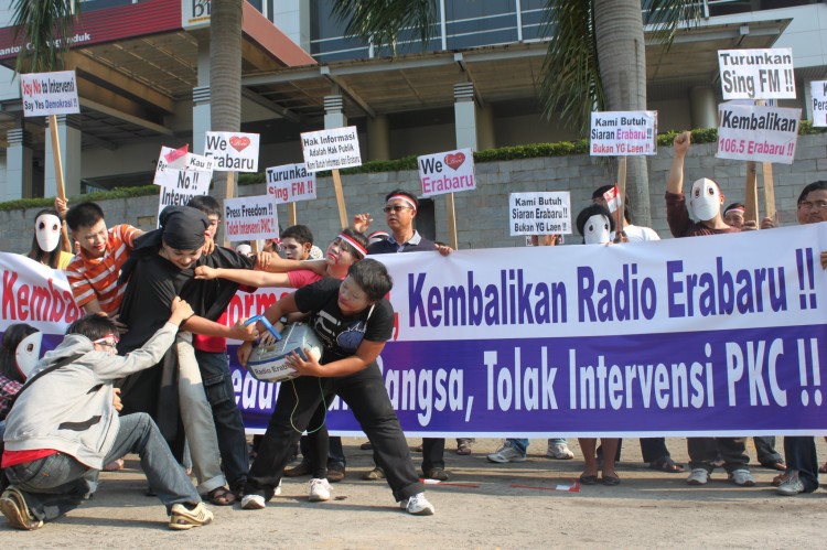 Fans of the Indonesian Radio Erabaru perform outside the headquarters of Sing FM a re-enactment of the forced shutdown of the station by government authorities on Sept. 13, as fellow protesters hold placards and banners that call for the restoration of Ra (Courtesy of Radio Erabaru)