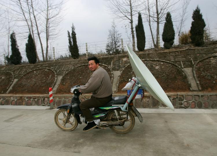 A Chinese man carries a TV satellite dish by motorcycle in 2005 in Jinzhai county, Anhui Province of China. (Cancan Chu/Getty Images)