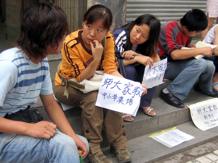 College students and graduates sit by a sidewalk