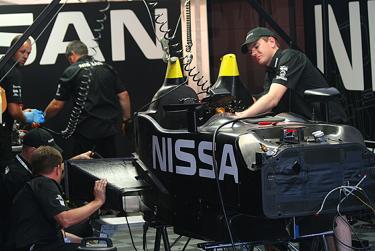 The DeltaWing's crew works to repair the damaged prototype. The driver's roll hoop shows the damage it sustained when it hit the pavement. (James Fish/The Epoch Times)