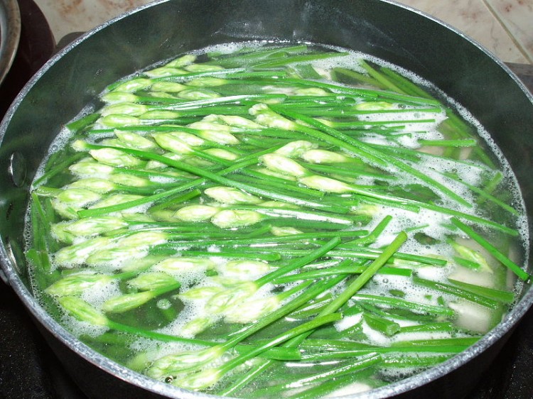 A saucepan containing cooking garlic chive flowers and soft tofu. (Photo by Le Hoan Nha)