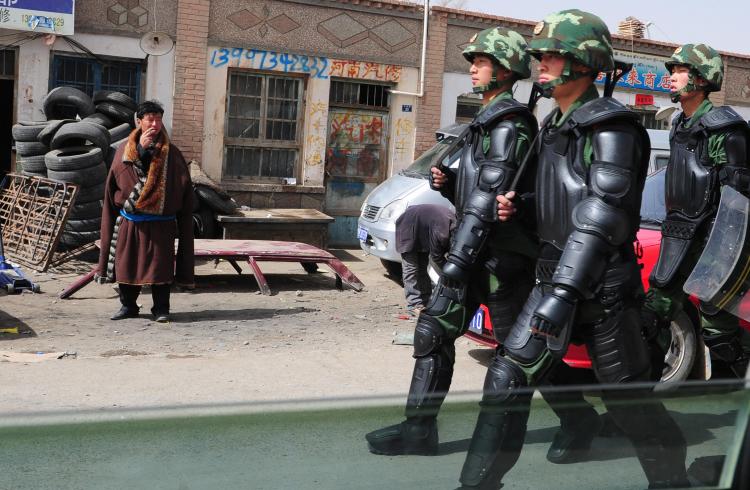 A Tibetan man (L) in traditional clothing watches as Chinese paramilitary troops in riot gear march along the streets of Guomaying,on the Tibetan plateau.(Frederic J. Brown/AFP/Getty Images)