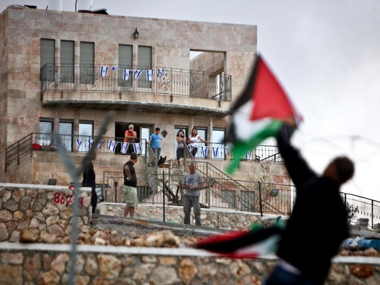 Israeli settlers from the settlement of Har Gilo, built on the land of the village of Walajeh near Bethlehem, look at a Palestinian man attaching his national flag on a fence surrounding the settlement on March 16, 2010. (MUSA AL-SHAER/AFP/Getty Images)