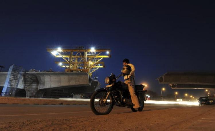 A Indian motorcyclist talks on his mobile phone as work goes on at an under-construction elevated road in New Delhi on May 11, 2010 for the forthcoming 2010 Commonwealth Games. (Manpreet Romana/AFP/Getty Images)