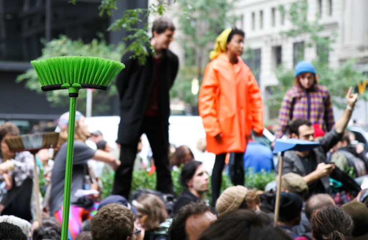 Occupy Wall Street protesters hold up brooms during the afternoon General Assembly before cleanup begins on Thursday in Zucotti Park.(Zack Stieber/The Epoch Times)