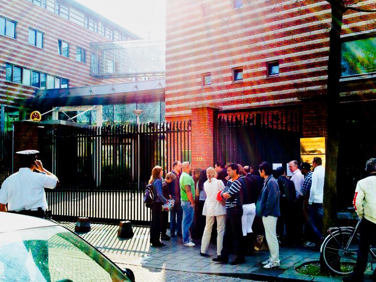 A crowd of visa applicants huddle around the closed gates of the Chinese Embassy in The Hague, across the road from the group of protesters, April 24, 2009. (The Epoch Times)