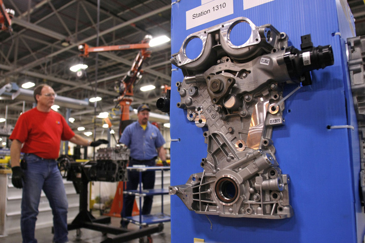 An engine part is displayed as GM workers demonstrate an assembly process