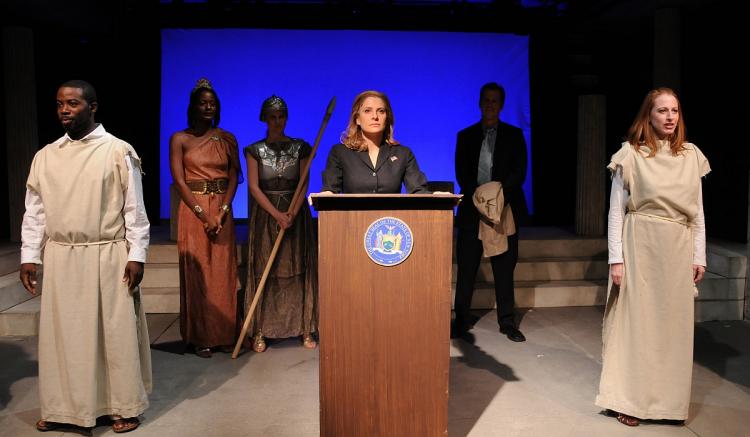 THE GREEKS AND POLITICS: (L-R) Charlie Hudson III, Victoire Charles, Heidi Armbruster, Mia Barron (at podium), Darren Pettie (in shadows), and Josie Whittlesey in a play about Hillary Clinton. (Jim Baldassare)