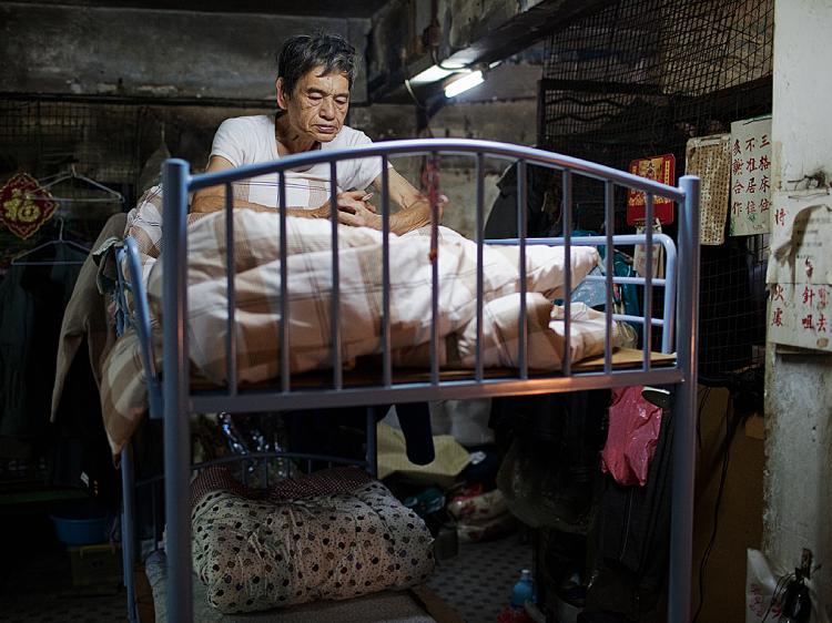 An elderly resident pauses as he smokes a cigarette in his bunk bed at Hong Kong's 'cage dwelling.' Thousands are unable to afford housing in the metropolis where the aging population is booming and the wealth gap is widening. (Daniel Berehulak/Getty Images)