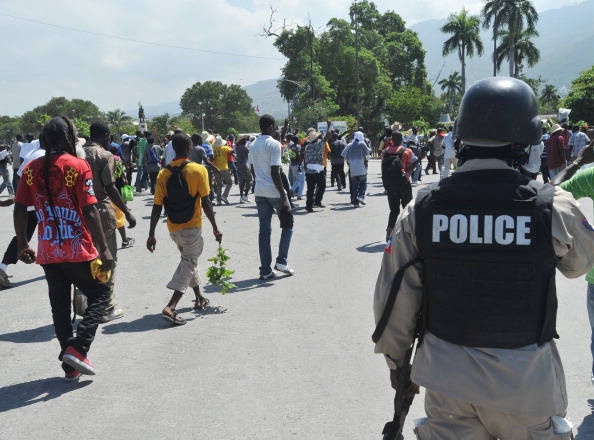 A Haitian policeman observes anti-government demonstrators marching in the streets of Port-au-Prince October 14, 2012 to protest the cost of living in Haiti. The demonstrators are calling for the resignation of President Michel Martelly. (Thony Belizaire/AFP/GettyImages)