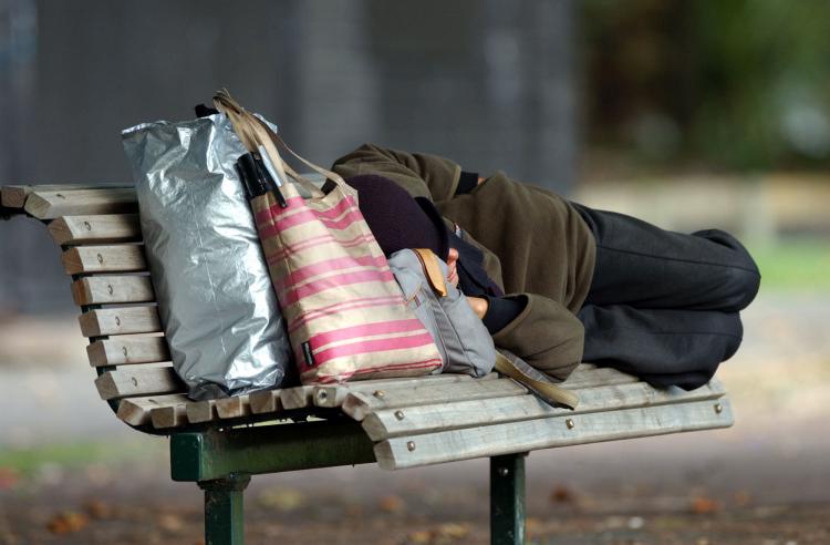 A homeless person sleeps on a park bench in Victoria Park,