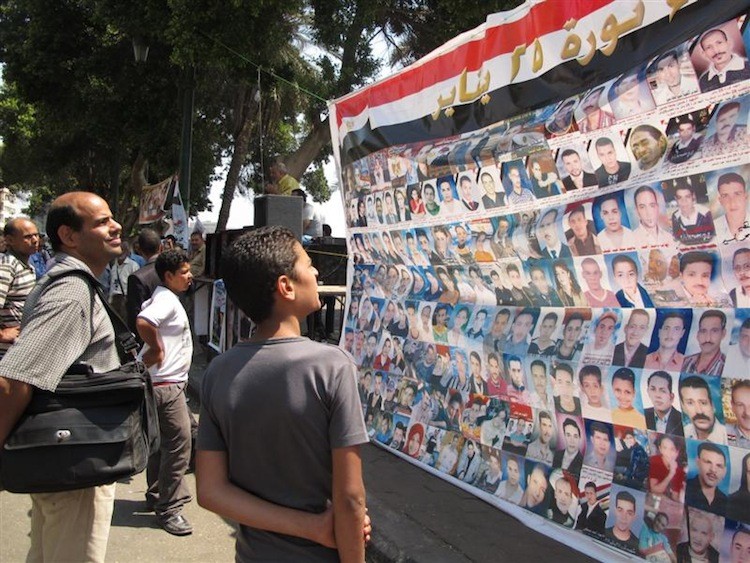 People look at the photos of those killed on Jan. 25. The banner was displayed next to the television building in Cairo, Egypt. The image is part of an exhibit and book that document this year's events in Egypt and Israel. (Yaira Yasmin/The Epoch Times)