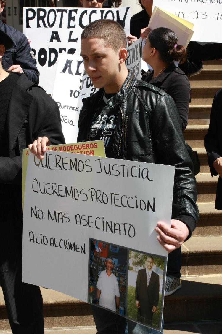 LOST TO VIOLENCE: The son of Juan Torres, who was shot in his bodega in October 2010, holds up photos of his father and calls for increased safety in the city's bodegas on Thursday at City Hall.  (Tara MacIsaac/The Epoch Times)