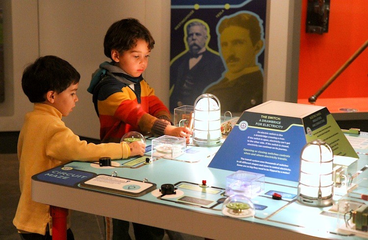 Patrick Rouse and Brian Kapfer enjoy an interactive exhibit at the new exhibition 'Electricity' at the New York Transit Museum. The faces behind them are electricity experts George Westinghouse and Nikola Tesla, who was known for inventing alternating current. (Zack Stieber/The Epoch Times)