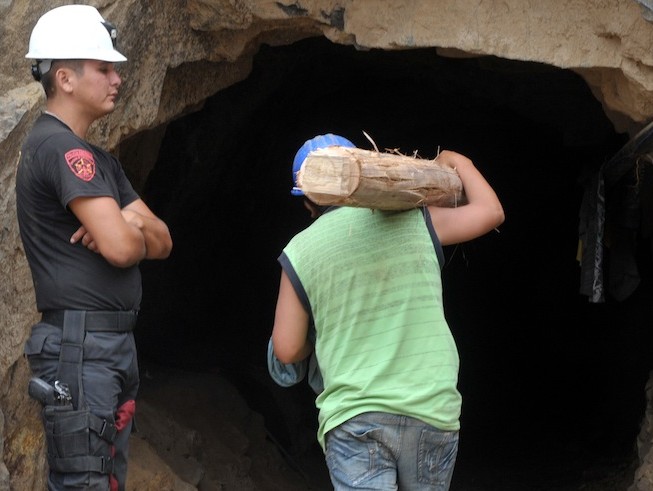 A policeman stands guard as a rescuer carries a timber post into the mine for use as a tunnel support during an operation to rescue nine miners at the Cabeza de Negro copper mine. (Cris Bouroncle/AFP/Getty Images)