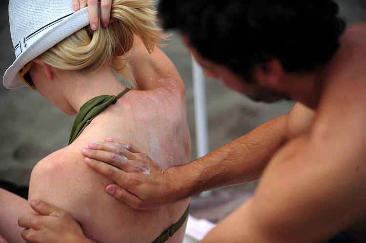 A sunbather applies sunscreen onto another