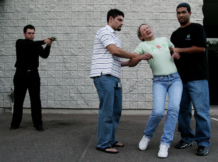 TASER International employee Evelina Self is held by employees Eric Rivera (L) and Charles Foster (R) as Taser Co-founder and President Tom Smith (far left) demonstrats the X26 Taser at the company's headquarters in Scottsdale, Arizona, on July 9, 2004. The X26, used by law enforcement and branches of the military, fires two metal probes. (Jeff Topping/Getty Images) 