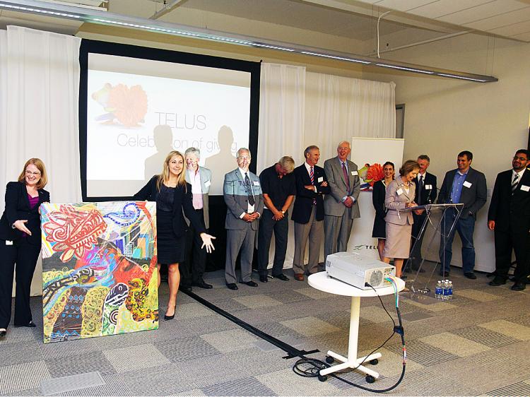 Telus employee and Telus Toronto Community Board member Jennifer Kirner (left), and Telus employee Megan Fielding (second left) unveil the artwork commissioned by Telus and done by a youth artist from SKETCH, a Toronto art studio for street-involved youth, while Telus Toronto Community Board members look on. The Board, Telus employees, and 60 charities attended the inaugural TELUS Celebration of Giving in Toronto where Telus announced $7.3 million in support of charities across the GTA. (Courtesy of Telus)