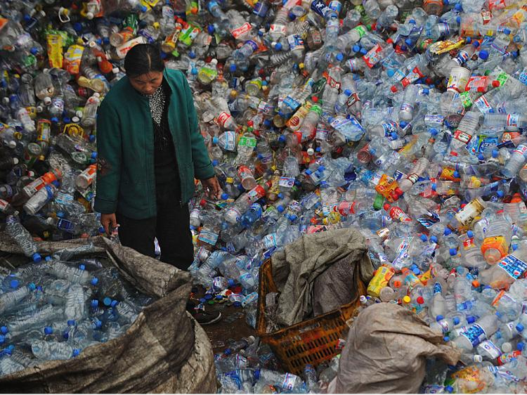 A woman stands amongst a huge pile of used plastic bottles at a plastics recycling mill which is ceasing production as the global financial crisis starts to bite in China's recycling industry on October 29, 2008 in Wuhan of Hubei Province, China. (China Photos/Getty Images)