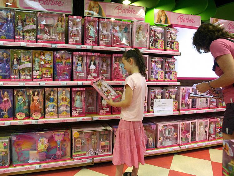 A young girl holds a Barbie doll next to a display of Barbie toys and accessories, made by Mattel. (Mark Ralston/AFP/Getty Images)